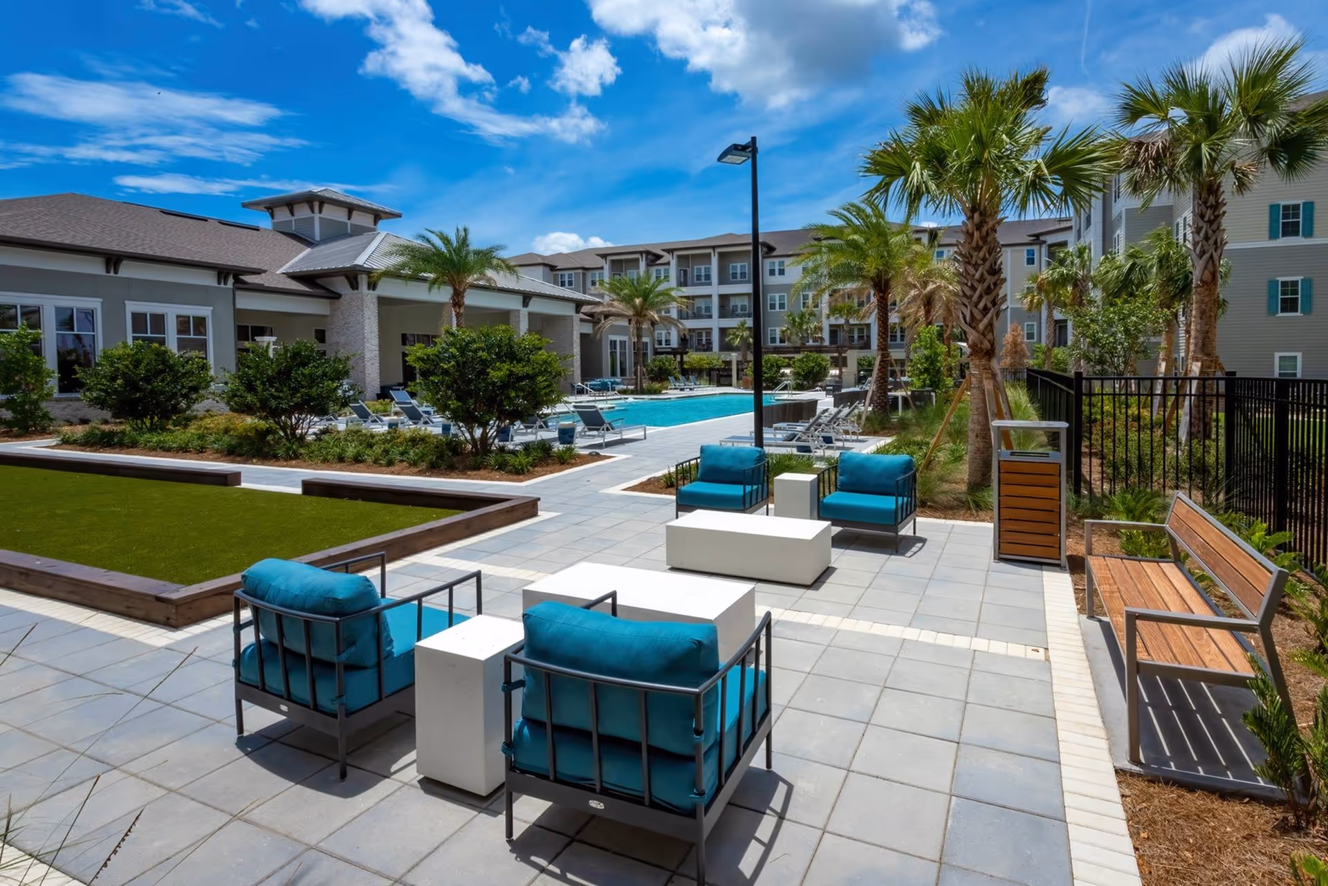 Courtyard pool area with turquoise cushioned lounge chairs, palm trees, and surrounding residential buildings.