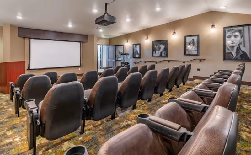 Small movie theater-style media room with rows of reclining seats facing a projection screen and ceiling projector.