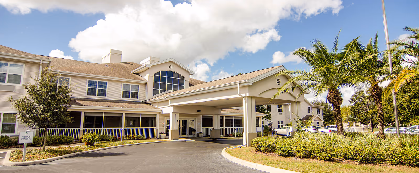 Exterior view of a senior living facility named Brookdale Highlands with a covered entrance, palm trees, and a parking area under a partly cloudy sky.