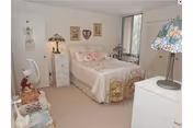 Small feminine bedroom with a double bed dressed in floral bedding, a bedside table and dresser with decorative lamps, and wall decorations.