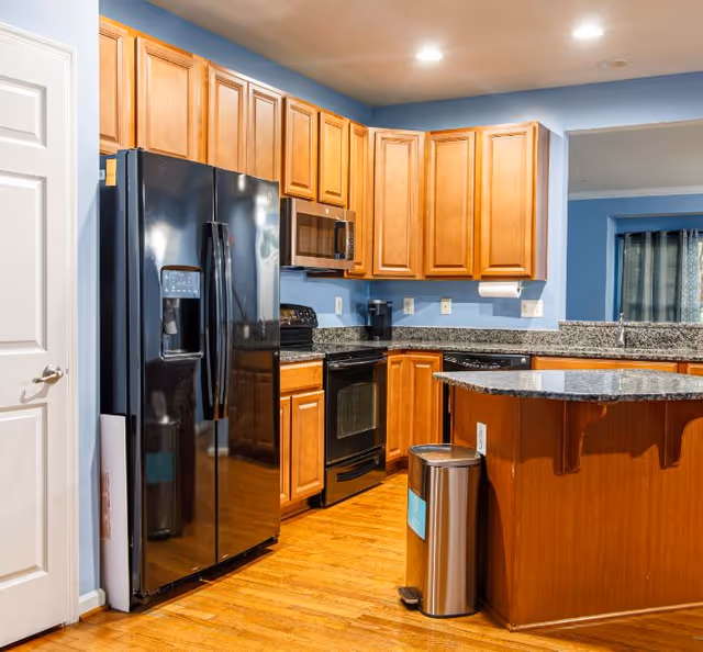 Modern kitchen with wooden cabinets, black appliances, granite countertops, a center island, and hardwood floors.
