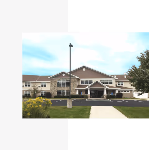 Front exterior view of Cedar Crest Estate, a two-story building with a combination of stone and siding facade, a covered entrance, and a parking lot in front with a sidewalk leading to the entrance. There are some trees and shrubs around the building.