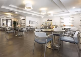 Bright communal dining room with round tables, chairs, a buffet counter and modern ceiling lights.