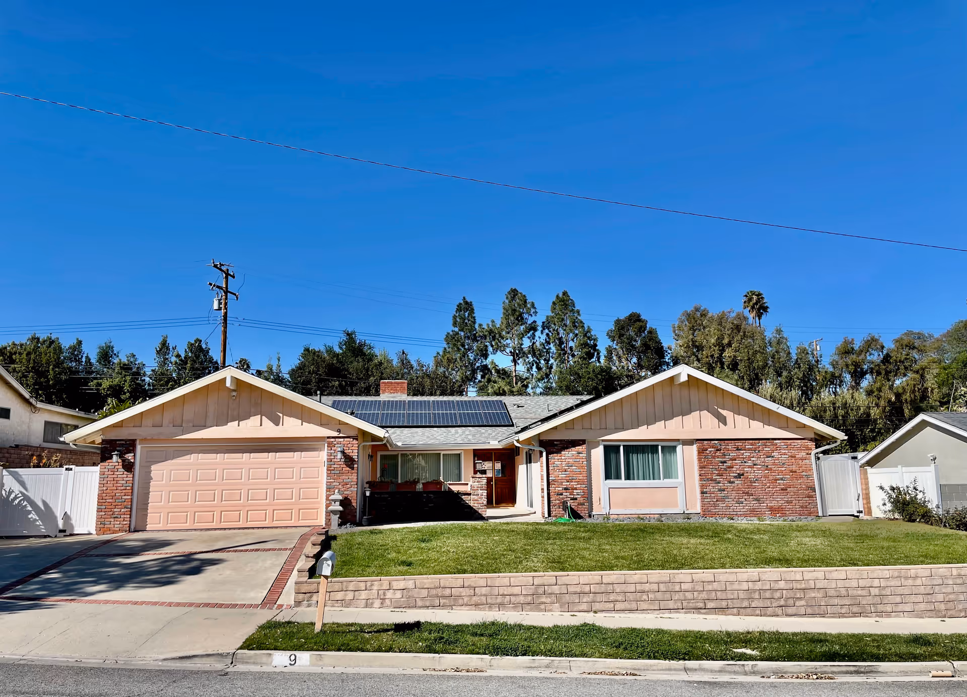 Single-story brick and stucco ranch house with an attached two-car garage, front lawn, and solar panels on the roof.