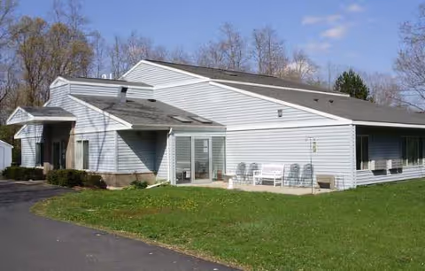 Waupaca Elder Care Home exterior: a single-story light-blue building with front entrance and outdoor seating.