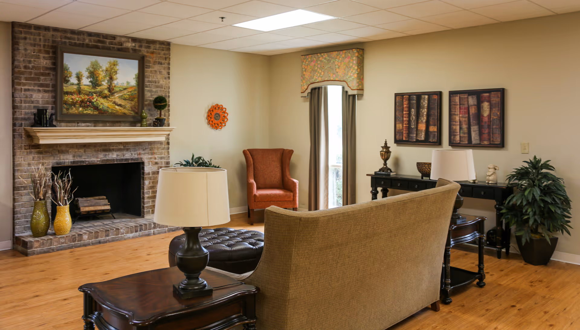 Cozy living room with a brick fireplace, sofa and armchair, lamps, artwork, and wood flooring.