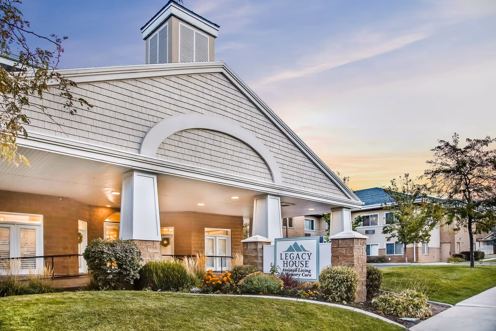 Front entrance of Legacy House assisted living facility with a covered portico, sign, and landscaped lawn.