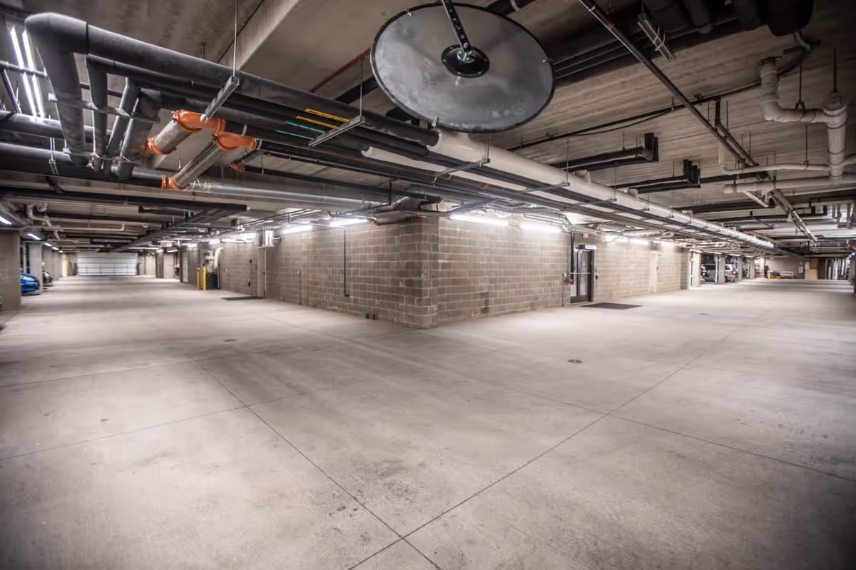 Spacious underground parking garage with concrete floors, exposed ceiling pipes, and cinder block walls.