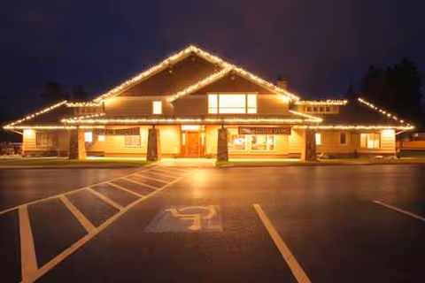 Night view of a warmly lit senior living facility front with string lights and handicap spaces.