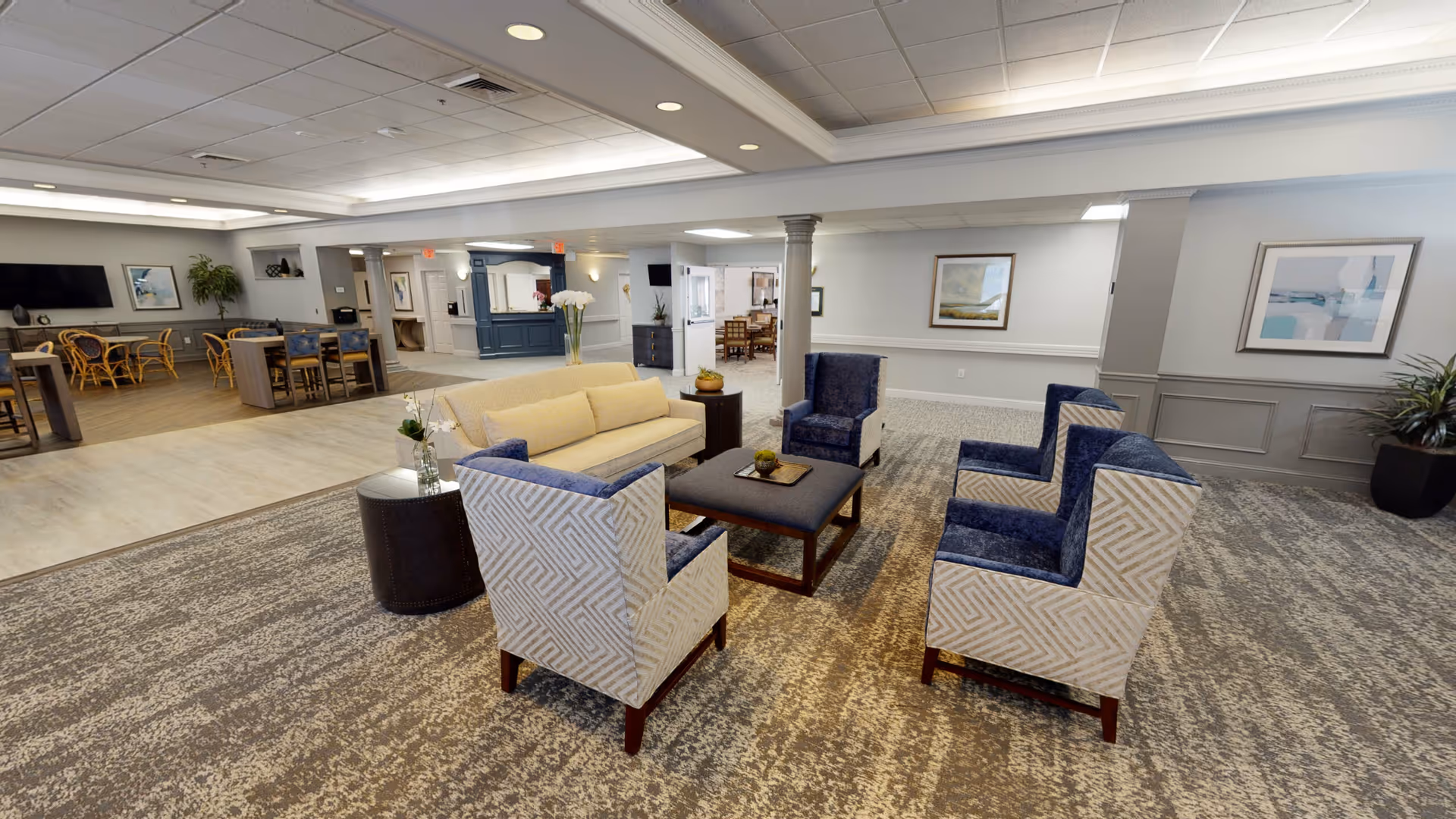 Spacious senior living common lounge with sofas, armchairs, a coffee table, and a dining area visible in the background.