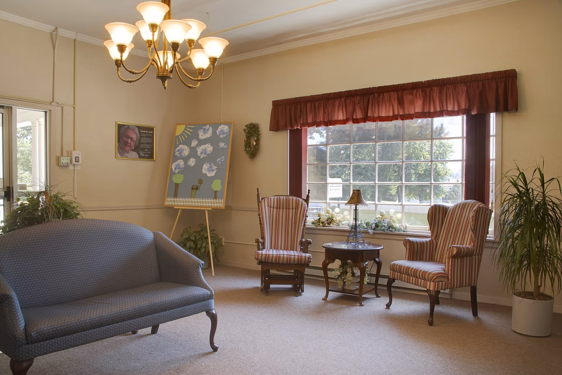 A bright sitting area with a blue sofa, two striped armchairs, a small round table, and a large window with a valance.