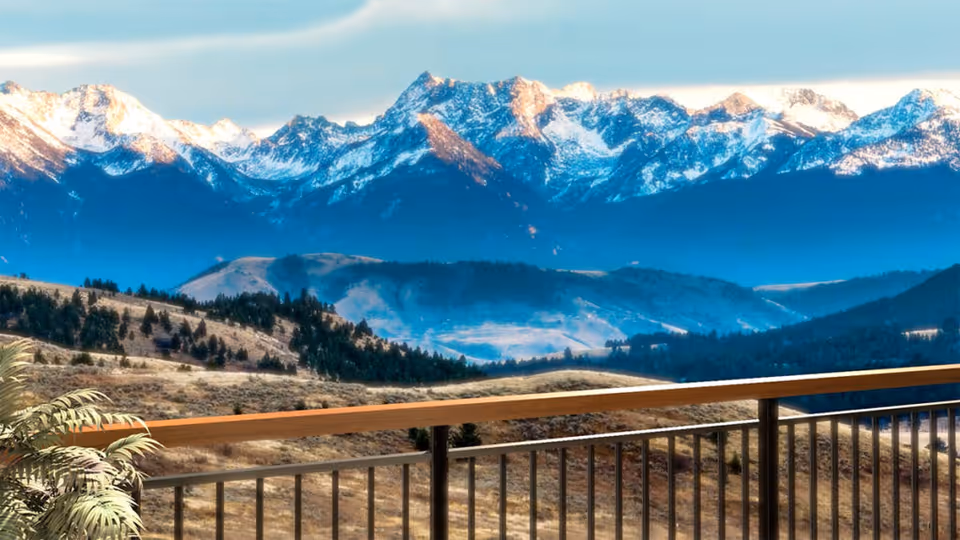 View from a balcony overlooking a scenic landscape with rolling hills and a range of snow-capped mountains in the background under a clear sky.