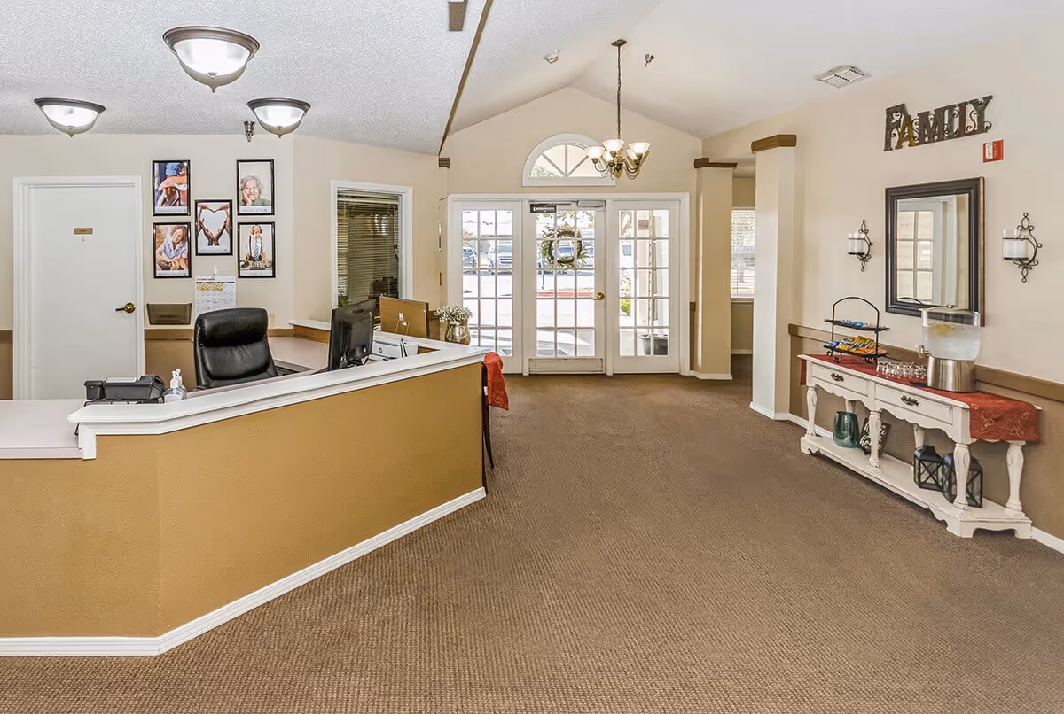 Reception lobby showing a front desk with chair and computer, decorative console table, and glass double entrance doors.