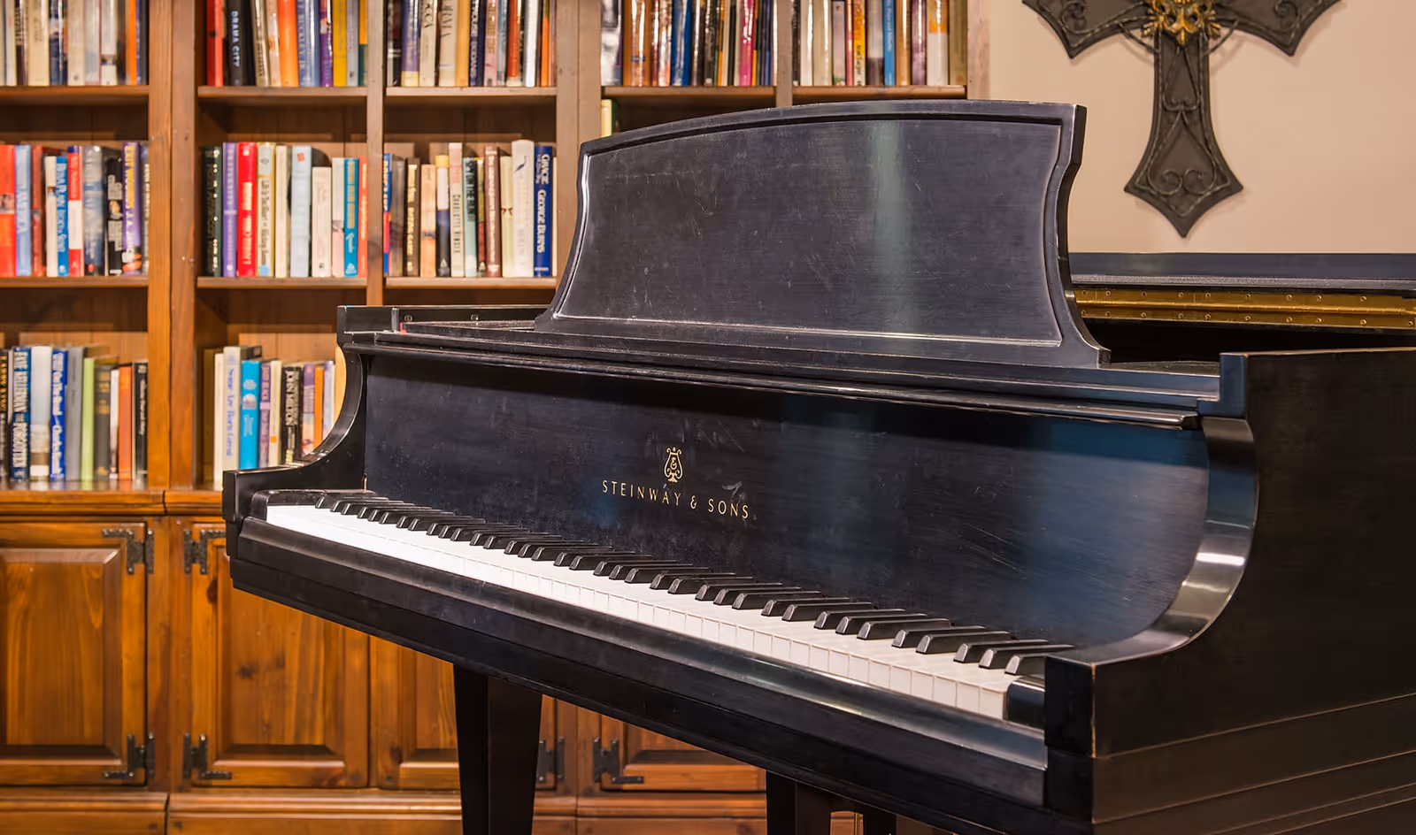 A black Steinway grand piano positioned in front of a wooden bookshelf filled with books in an interior room.