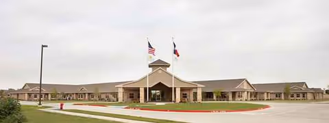 Wide exterior view of a single-story senior living facility with flagpoles and entrance.