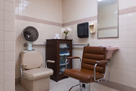 A clean and functional bathroom space with a chair, mirror, and small cabinet.