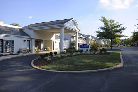 Front entrance of a senior living facility with a covered porte-cochere, circular driveway, landscaped island and a sign near the entrance.