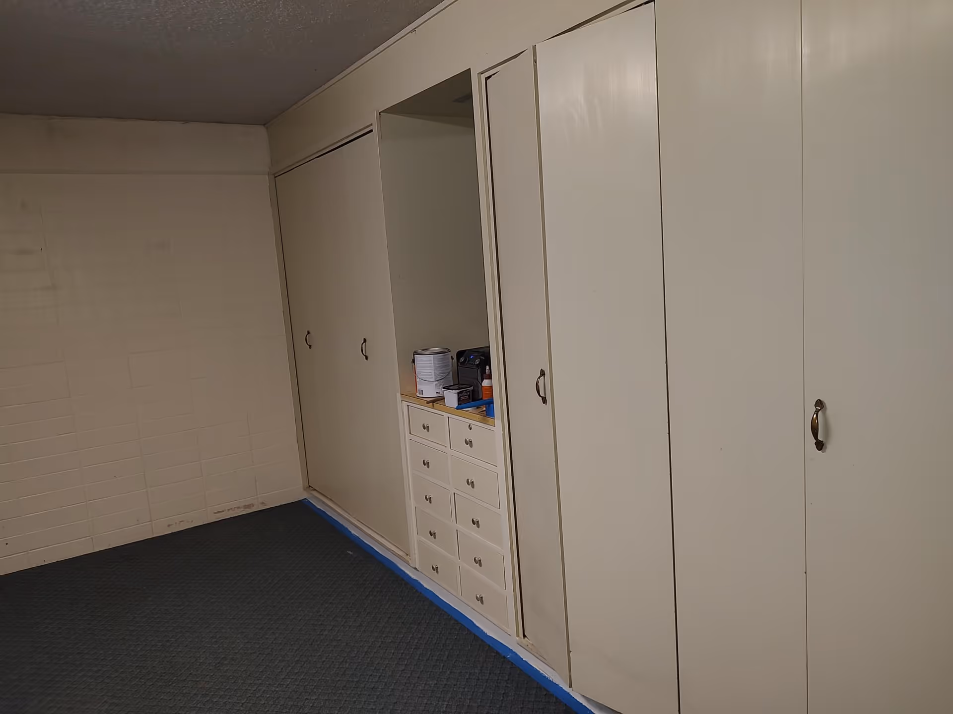 Carpeted interior room featuring a wall of built-in white closets and small drawers.