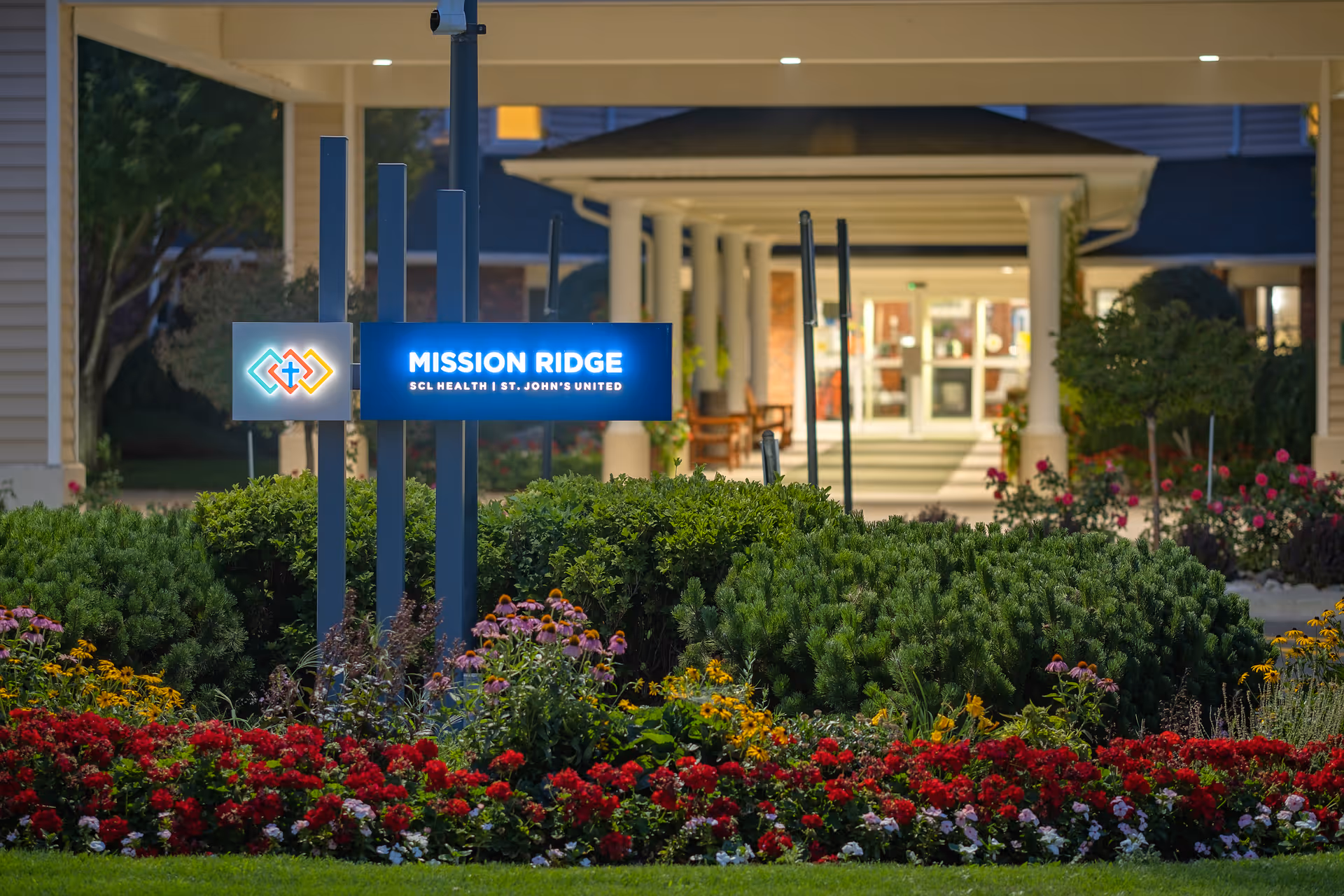 The sign for Mission Ridge at St. John's United, surrounded by colorful flowers and greenery.