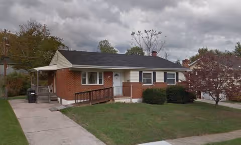 Single-story brick building with ramp, driveway, and a small front lawn under cloudy sky.