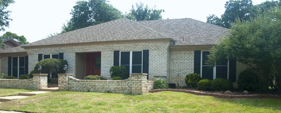 A single-story brick Satori Senior Care facility exterior with a manicured lawn and shrubs.