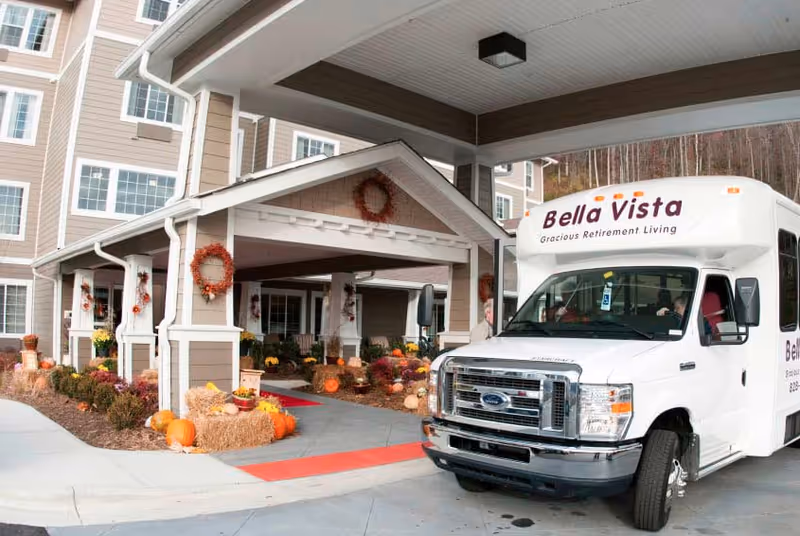 Exterior view of Bella Vista retirement living entrance with autumn pumpkins and a parked bus.