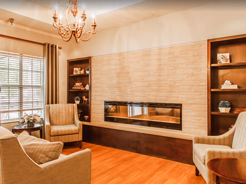 Bright seating area with upholstered armchairs, a horizontal fireplace set in a tiled wall, built-in shelving and a chandelier.