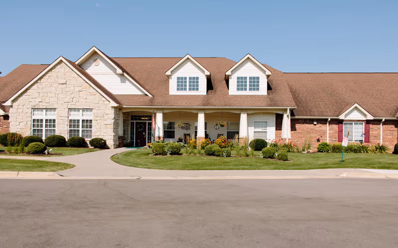 Front view of a single-story brick and stone residential building with dormer windows, a covered porch, and landscaped lawn.