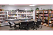 A bright community library with bookshelves along the walls and a rectangular table surrounded by chairs.