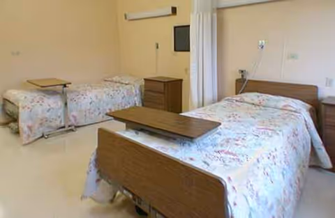 Two twin beds with floral bedding and privacy curtains in a shared senior living bedroom.