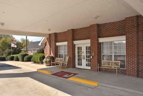 Brick building entrance to senior care center with double doors and benches under covered driveway.