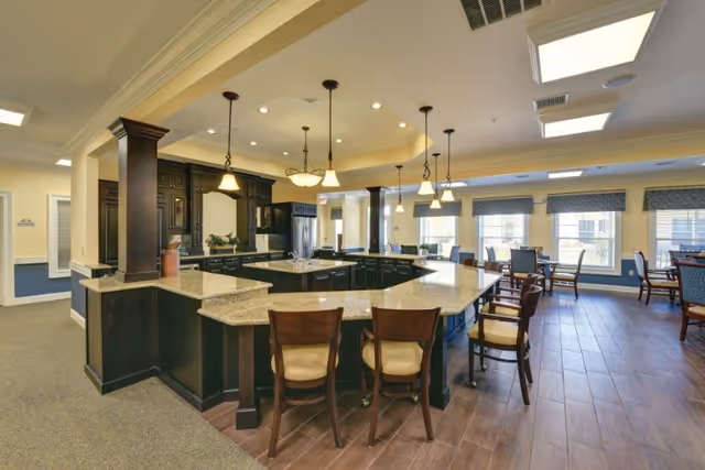 Spacious communal kitchen and dining area with a large granite-topped island, pendant lights, bar stools, and dining tables by windows.