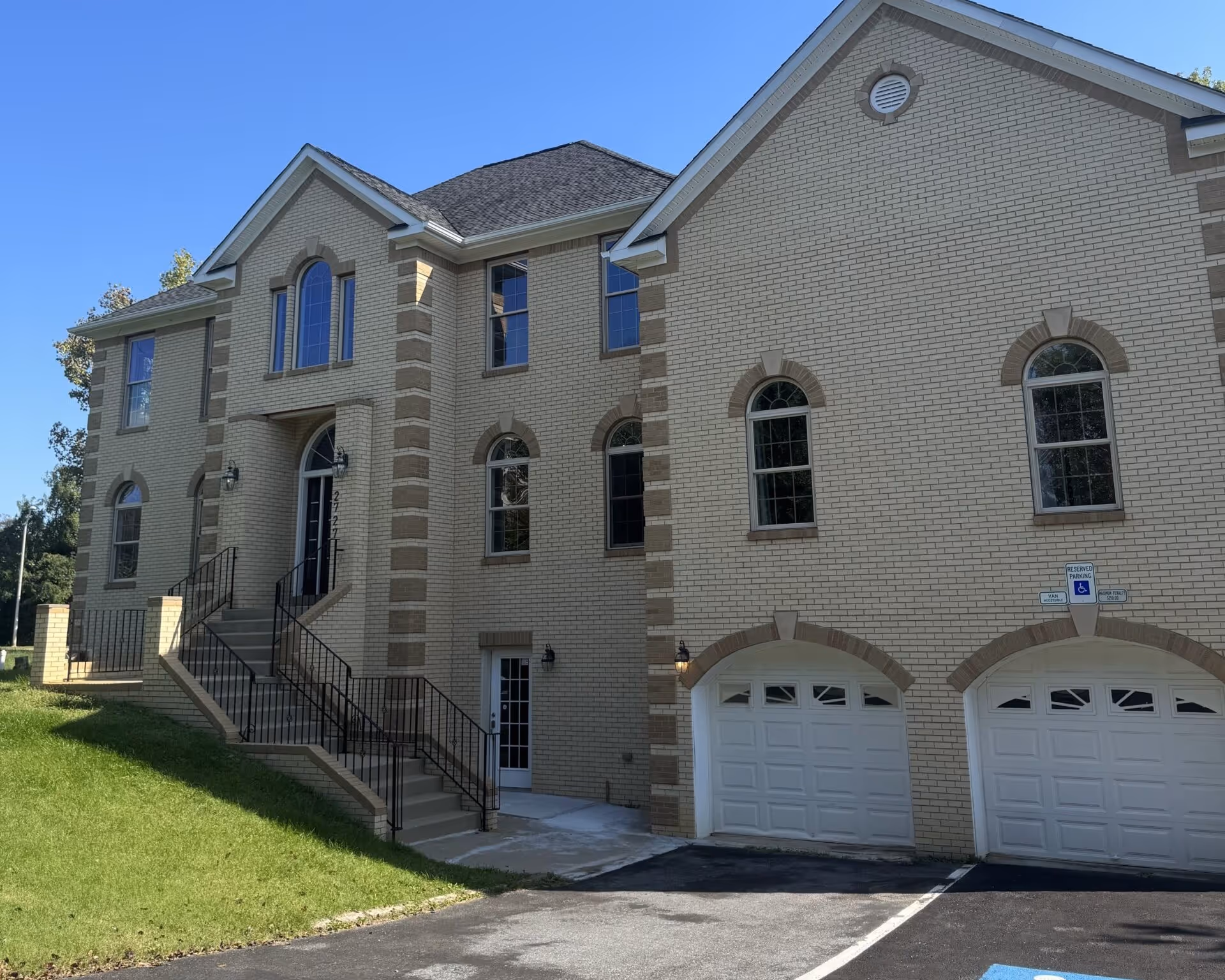 Exterior view of a beige brick assisted living building with arched windows and entry stairs