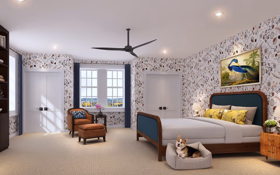 A spacious bedroom with patterned wallpaper featuring botanical designs. The room has a large bed with a wooden frame and blue upholstered headboard, decorated with yellow pillows. A small dog is lying in a pet bed at the foot of the bed. There is a wooden nightstand with a lamp and a plant, a brown armchair with a matching ottoman, and a small side table with a flower vase near a window with blue curtains. The room also features a ceiling fan and built-in shelving on the left side.