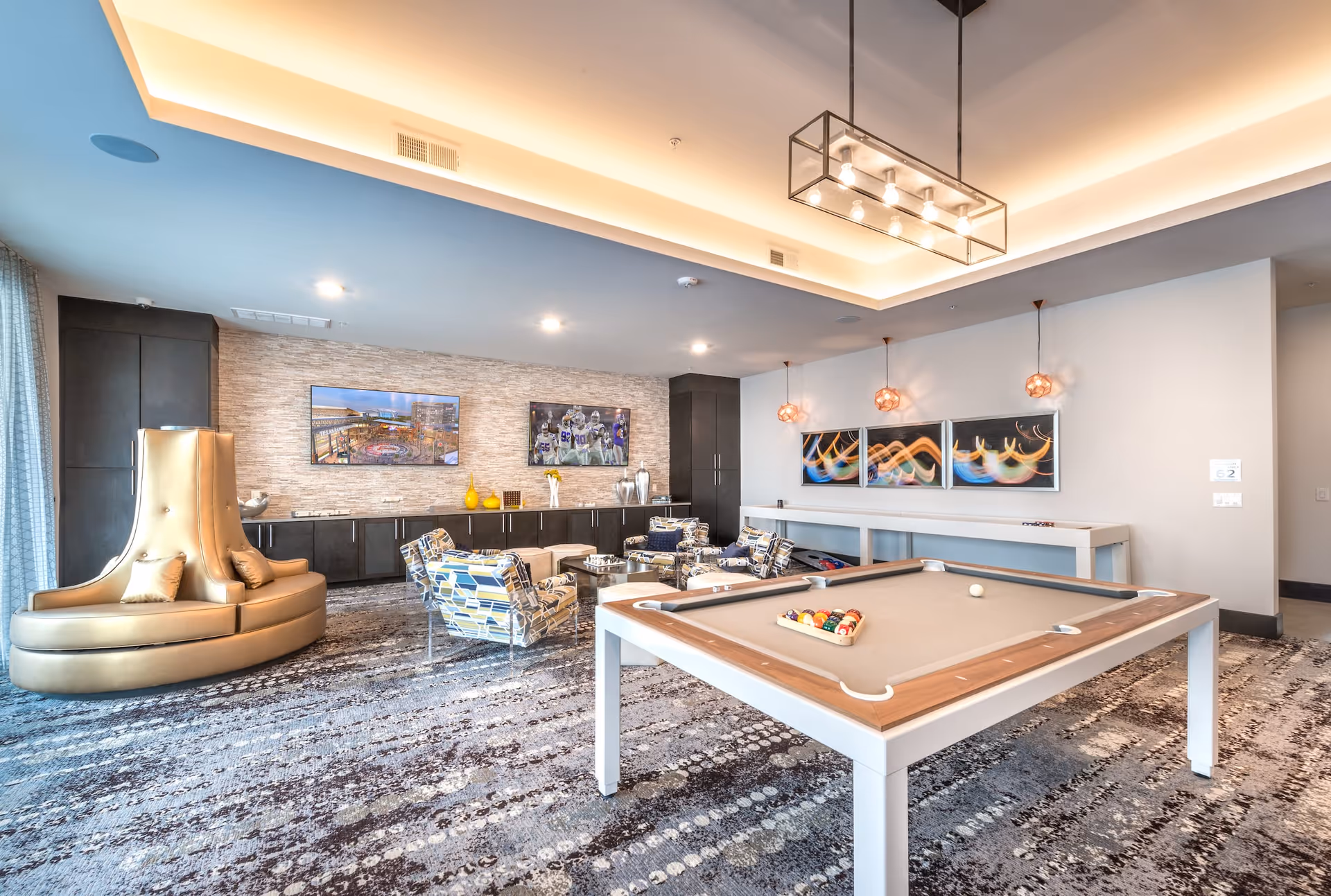 Modern senior living community game room with a pool table, seating area, and decorative lighting.