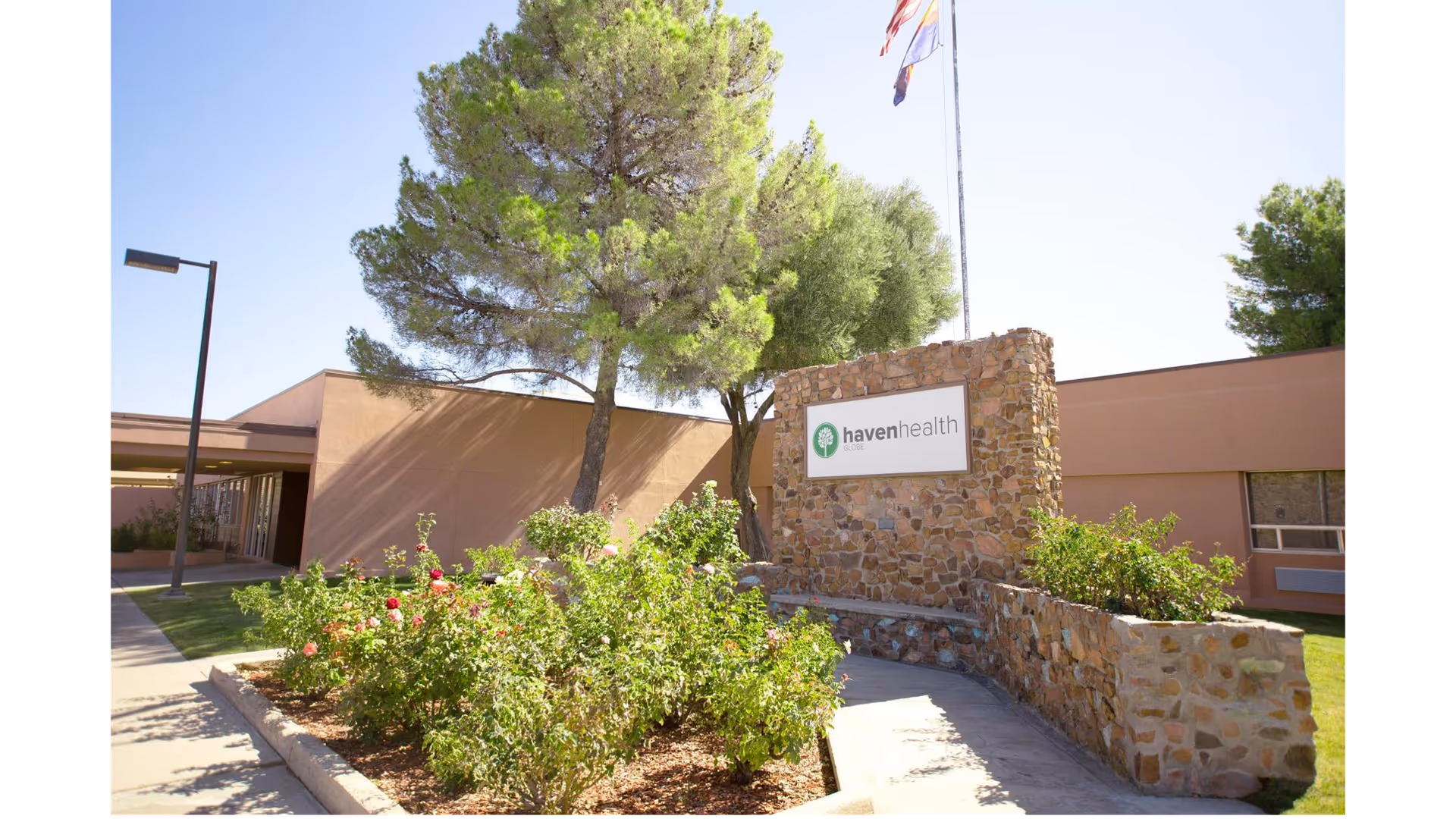 Exterior view of Haven Health Globe facility showing a stone sign with the facility's name, surrounded by greenery and trees under a clear blue sky.