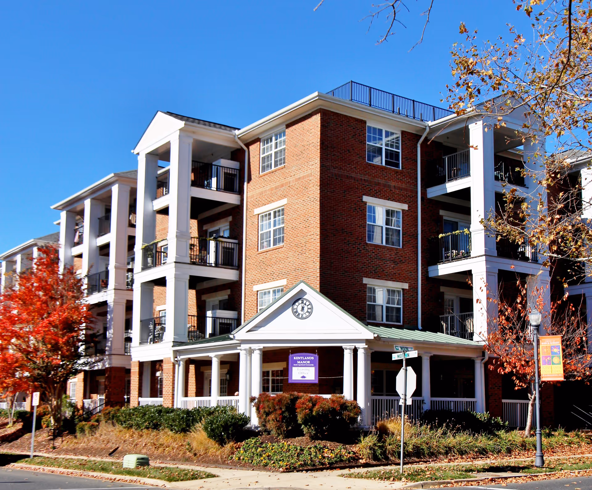 Brick multi-story senior living building with white columns, balconies, and a covered entrance displaying a Kentlands Manor sign.