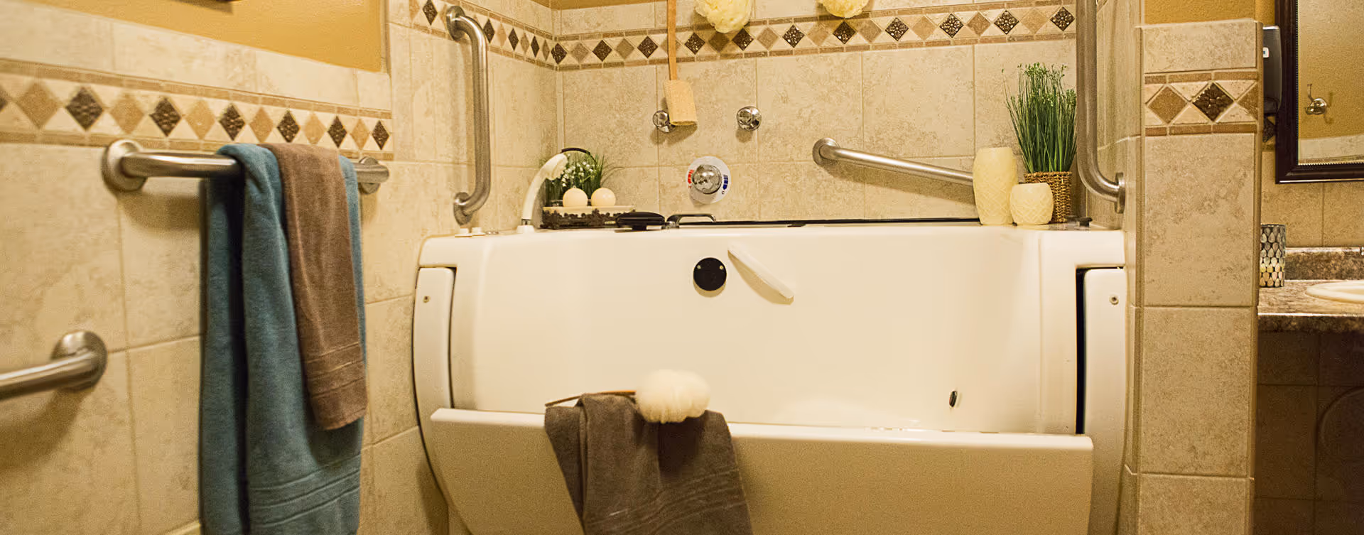 Walk-in bathtub in a tiled bathroom with grab bars, towels, and small decorative plants.