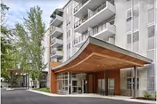 Modern multi-story senior building with glass entrance and a wooden canopy over the doorway.