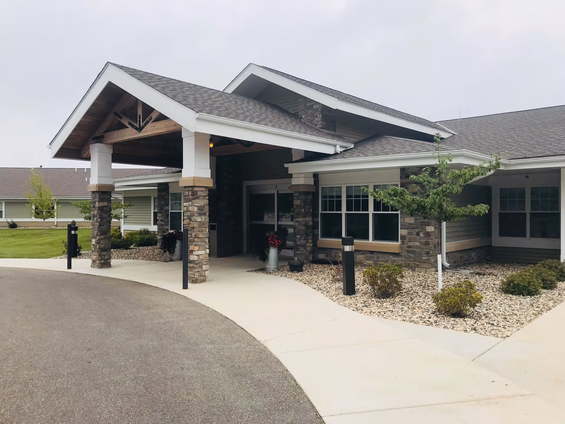 Covered front entrance of a single-story healthcare building with stone columns, a paved driveway, and landscaped rock beds.