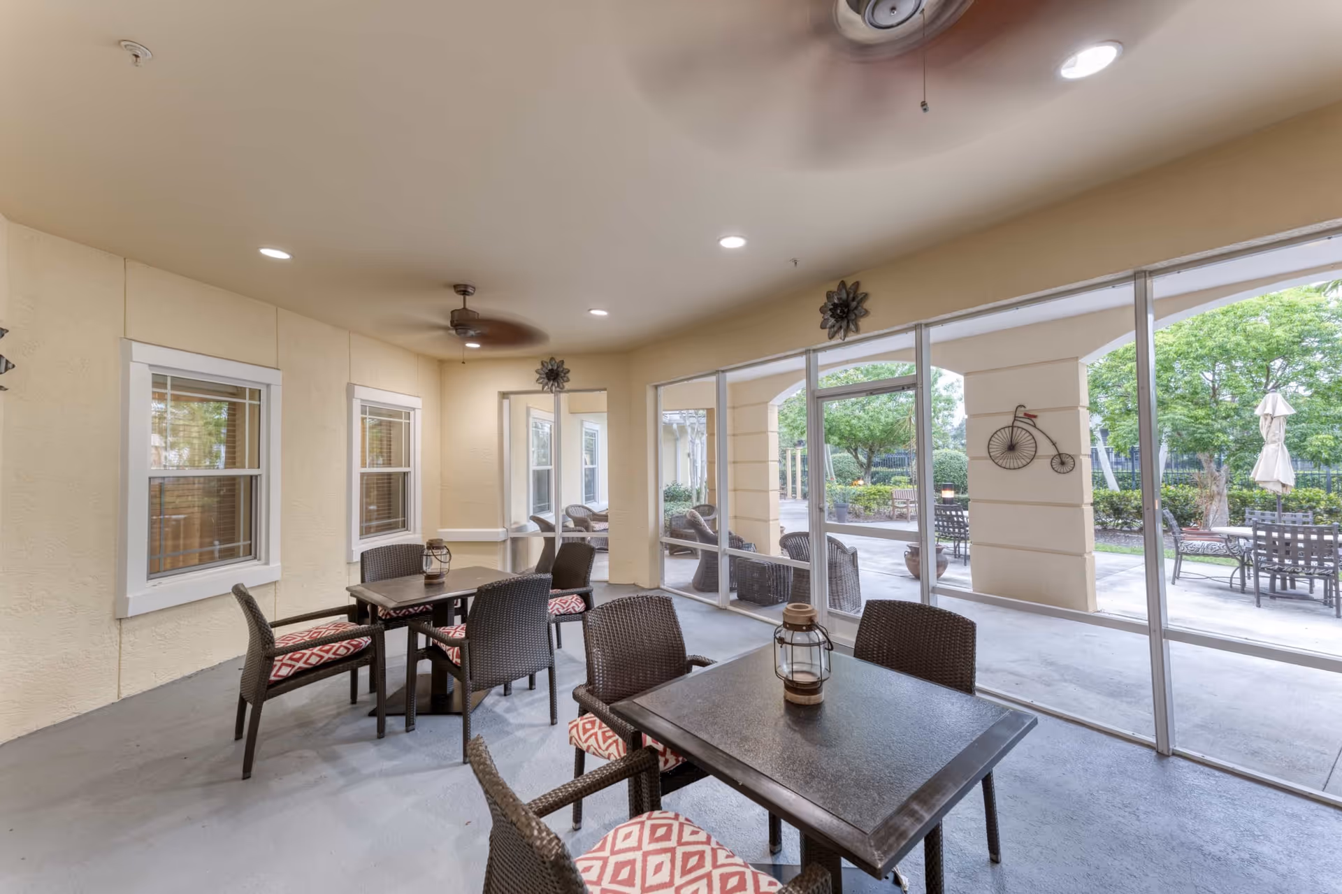 Covered indoor seating area with tables and chairs overlooking a landscaped outdoor patio through large windows.