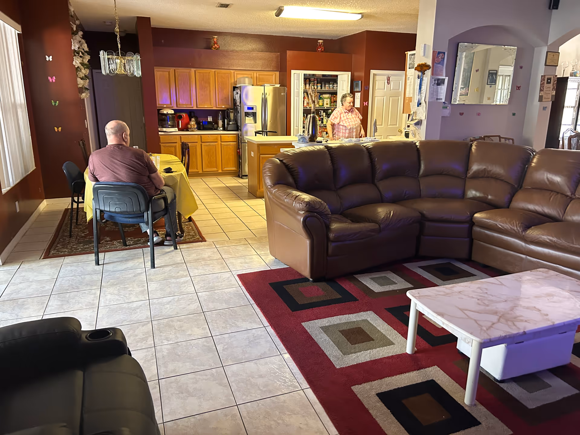 Spacious living area with a brown leather sectional, coffee table, and kitchen in the back.