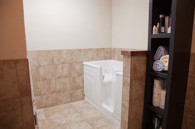 Tiled bathroom featuring a white walk-in bathtub and a shelving unit holding towels and toiletries.