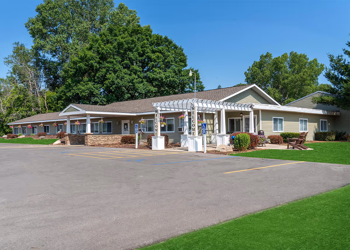 Single-story senior living facility with a welcoming entrance, sign pillars, and green lawn.