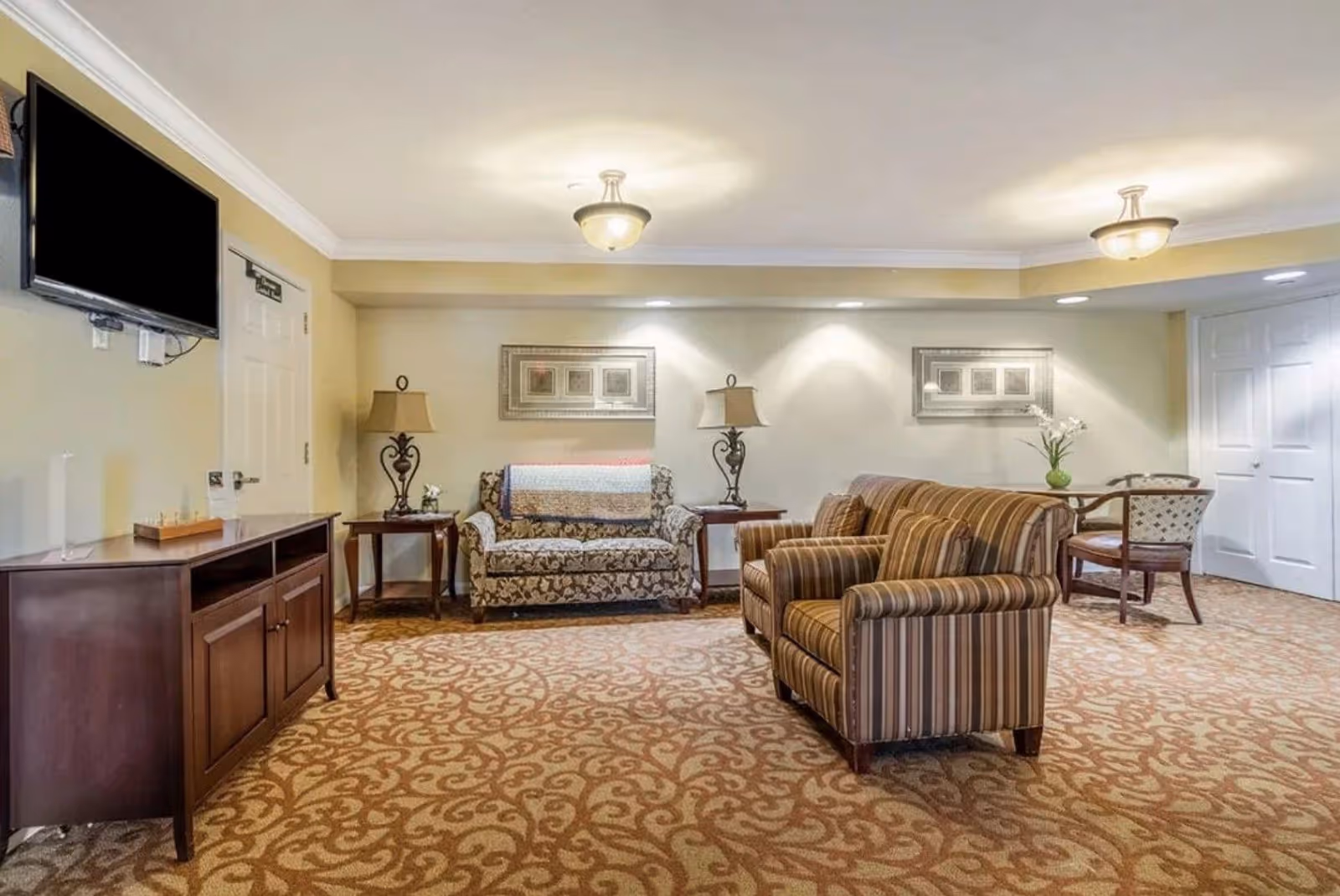 Common seating area with striped armchairs, a patterned sofa, side tables, lamps, wall art and a wall-mounted TV.