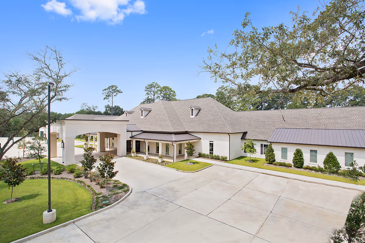 Front exterior of a single-story senior living building with a covered porte-cochere, landscaped grounds, and a paved driveway.