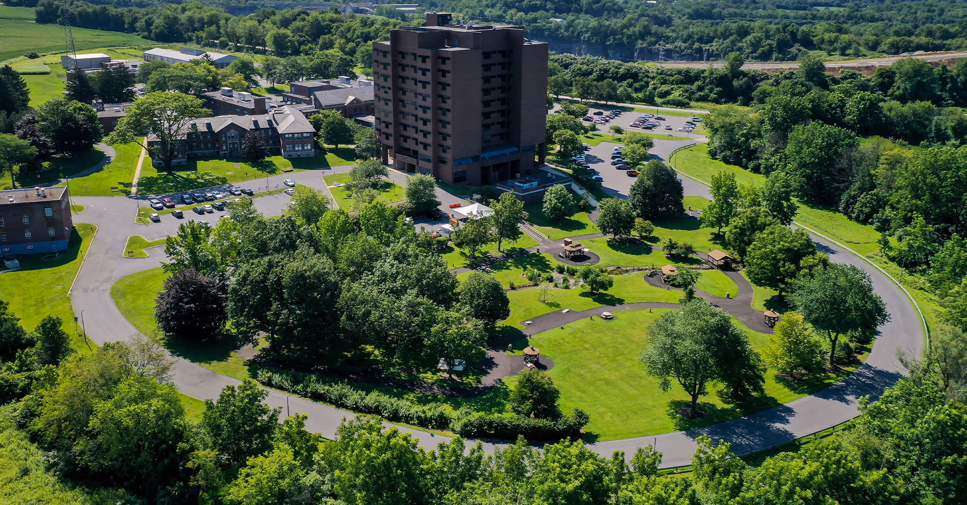 Aerial view of Gracedale Nursing Home facility showing multiple buildings surrounded by green lawns, trees, walking paths, and parking areas under a clear sky.