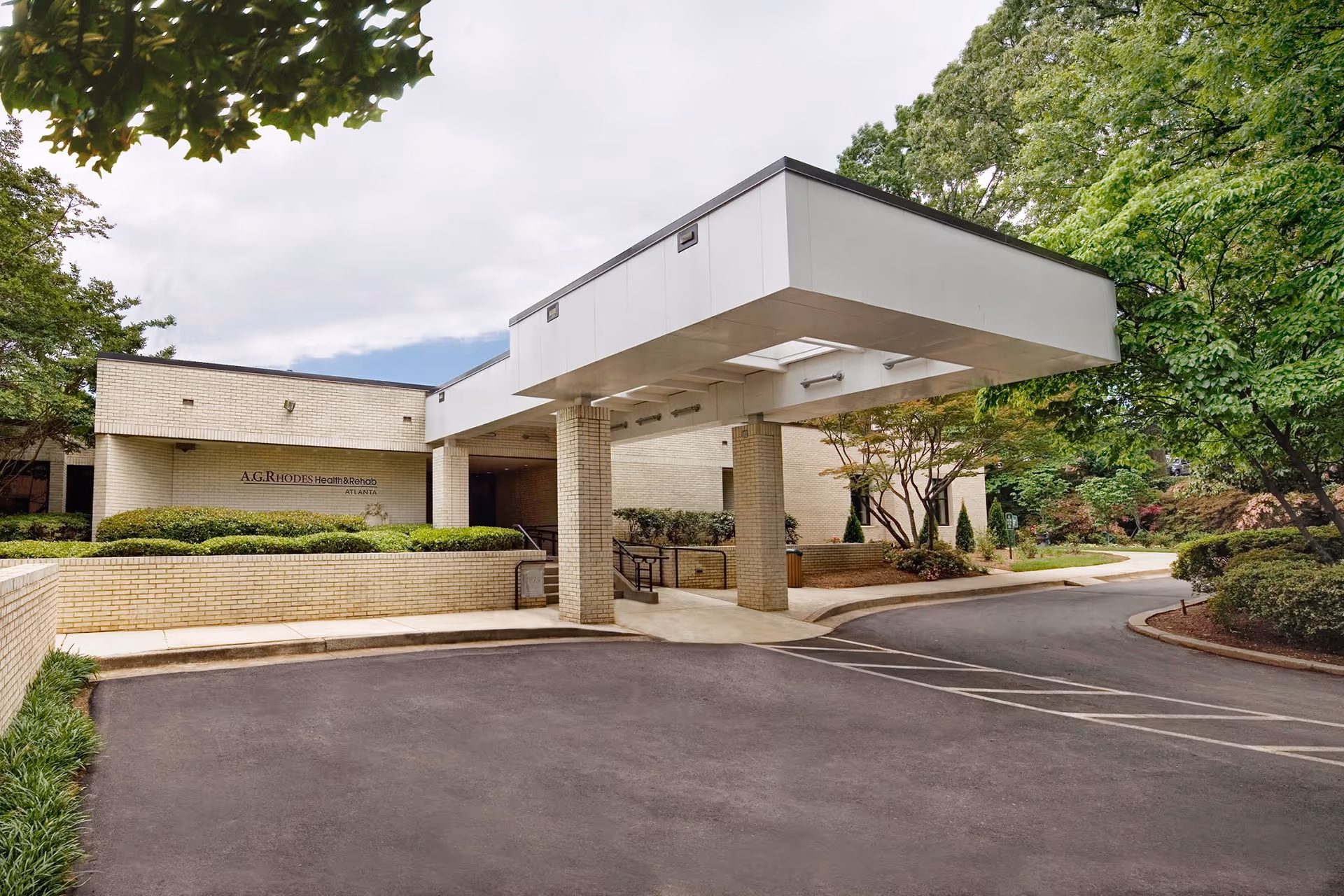 Exterior view of A.G. Rhodes Health & Rehab Atlanta building entrance with a covered drop-off area, surrounded by greenery and trees.