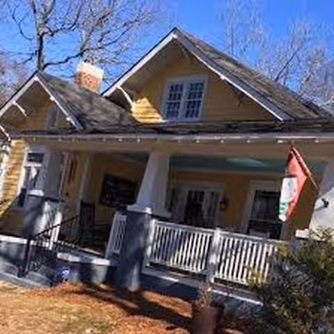 Yellow house-style senior care facility with a covered porch and white railing.