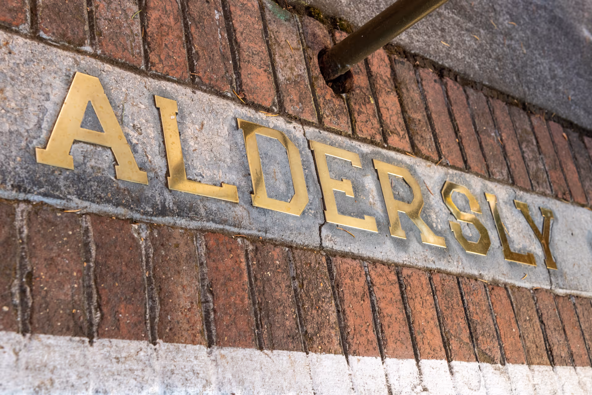 Brass letters spelling 'ALDERSLY' embedded in a stone band set into a brick entrance.